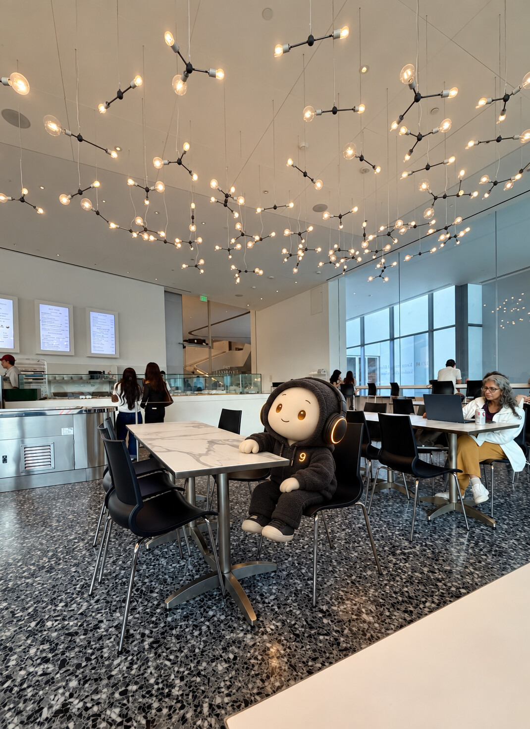 AI-edited vertical photograph inside Café Leonelli at the Museum of Fine Arts, Houston. Envoy9, a small ivory-faced character with amber eyes, a charcoal hoodie marked with a glowing 9, and black headphones, sits in the foreground black chair with one hand on a marble table, looking up at branching constellation-like lights. Café patrons and the bright modern interior remain visible.